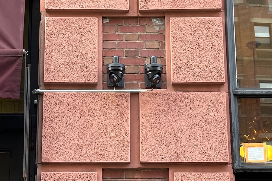 wo black outdoor surveillance cameras mounted on a red brick wall.