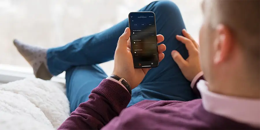 Persona sentada cerca de una ventana usando un smartphone con una interfaz oscura que muestra opciones como Quick Actions, My Dashboard y Your Workflows.
